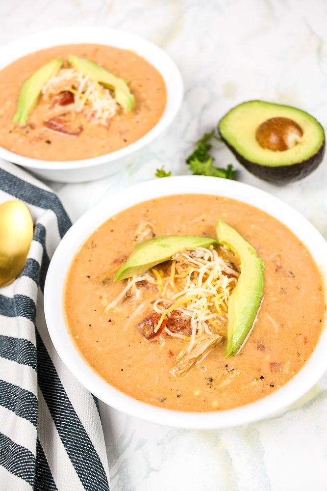 a bowl of Mexican chicken soup with cheese and avocado on top