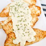 parmesan crusted fried fish with a creamy dijon mustard sauce on a white platter with a sprinkle of chives