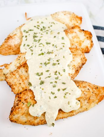 parmesan crusted fried fish with a creamy dijon mustard sauce on a white platter with a sprinkle of chives