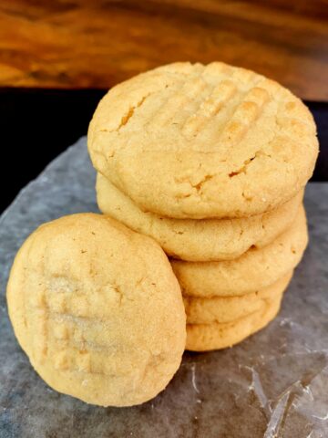 a pile of 4 old fashioned peanut butter cookies with one leaning against it