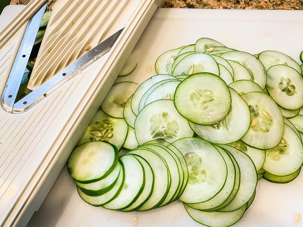 a mandoline on a cutting board with a sliced cucumber beside it