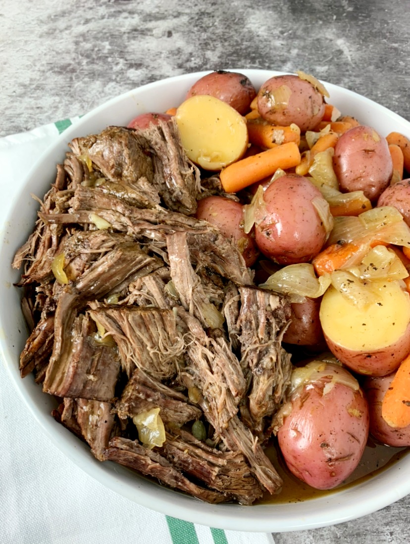 white round dish with shredded chuck roast and red potatoes and carrots