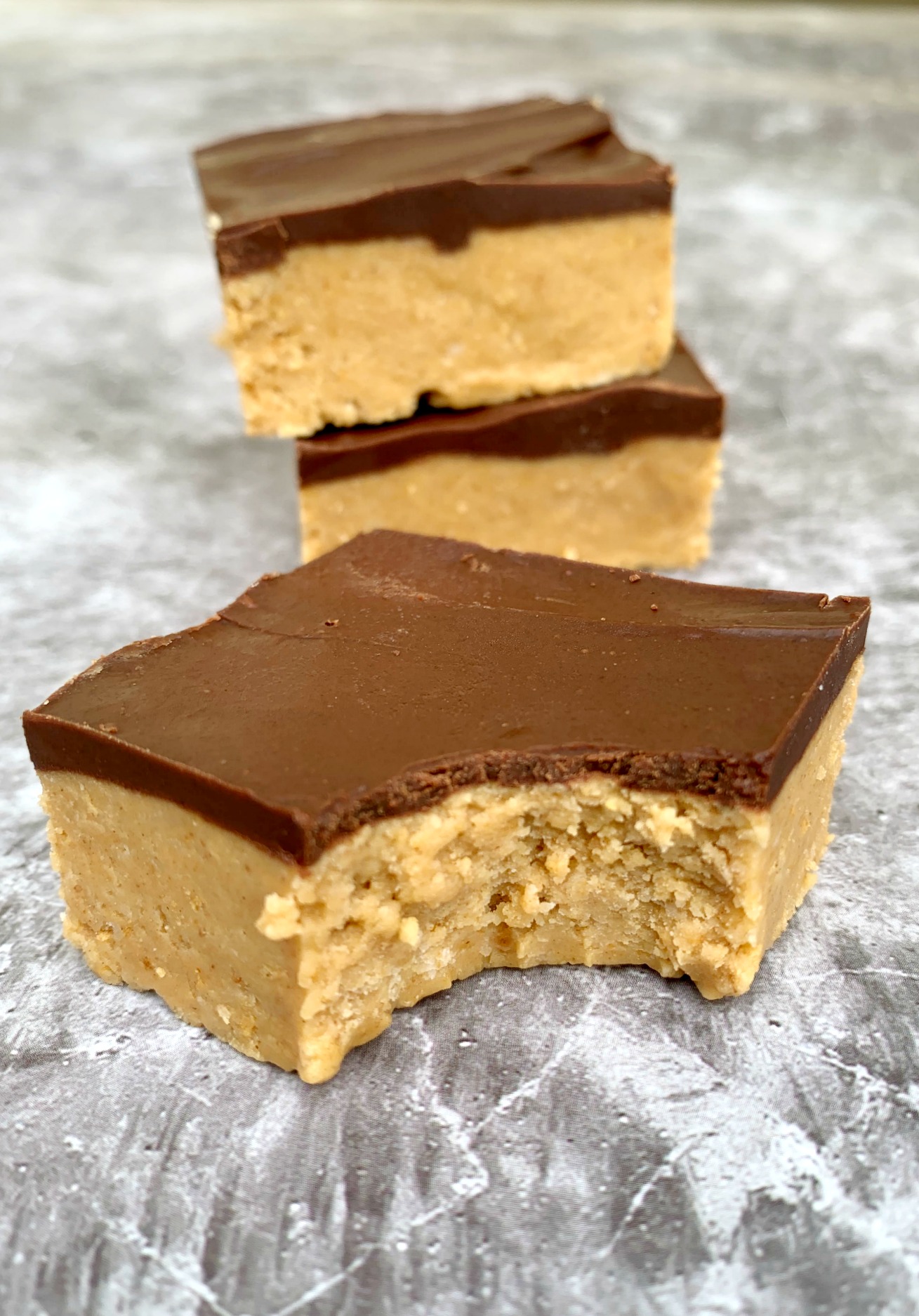 a peanut butter chocolate square with bite taken out of it and a stack of 2 bars in background