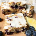 slices of lemon blueberry coffee cake on a cutting board with blueberries scattered around
