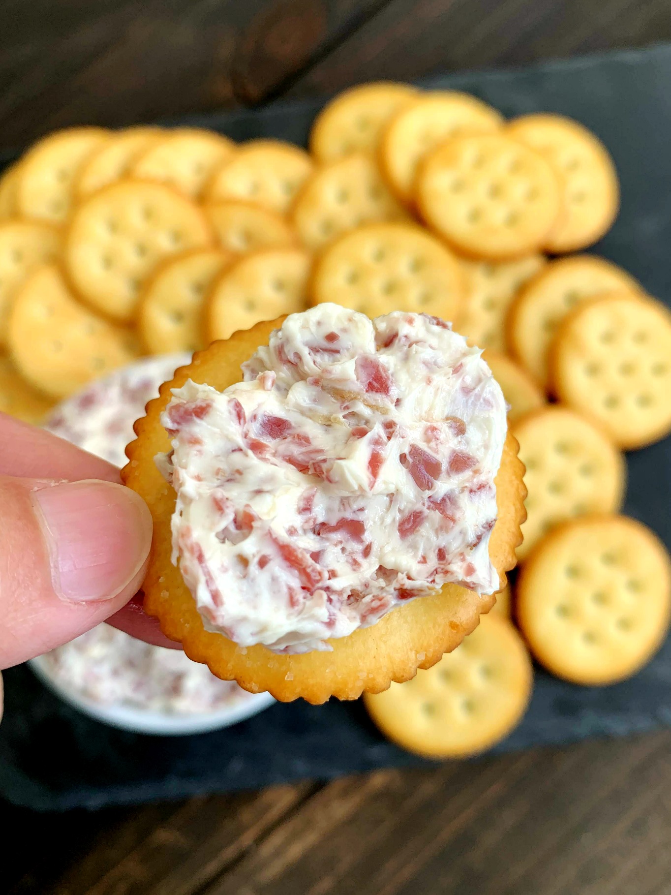 cracker smeared with chipped beef dip with a pile of crackers in the background