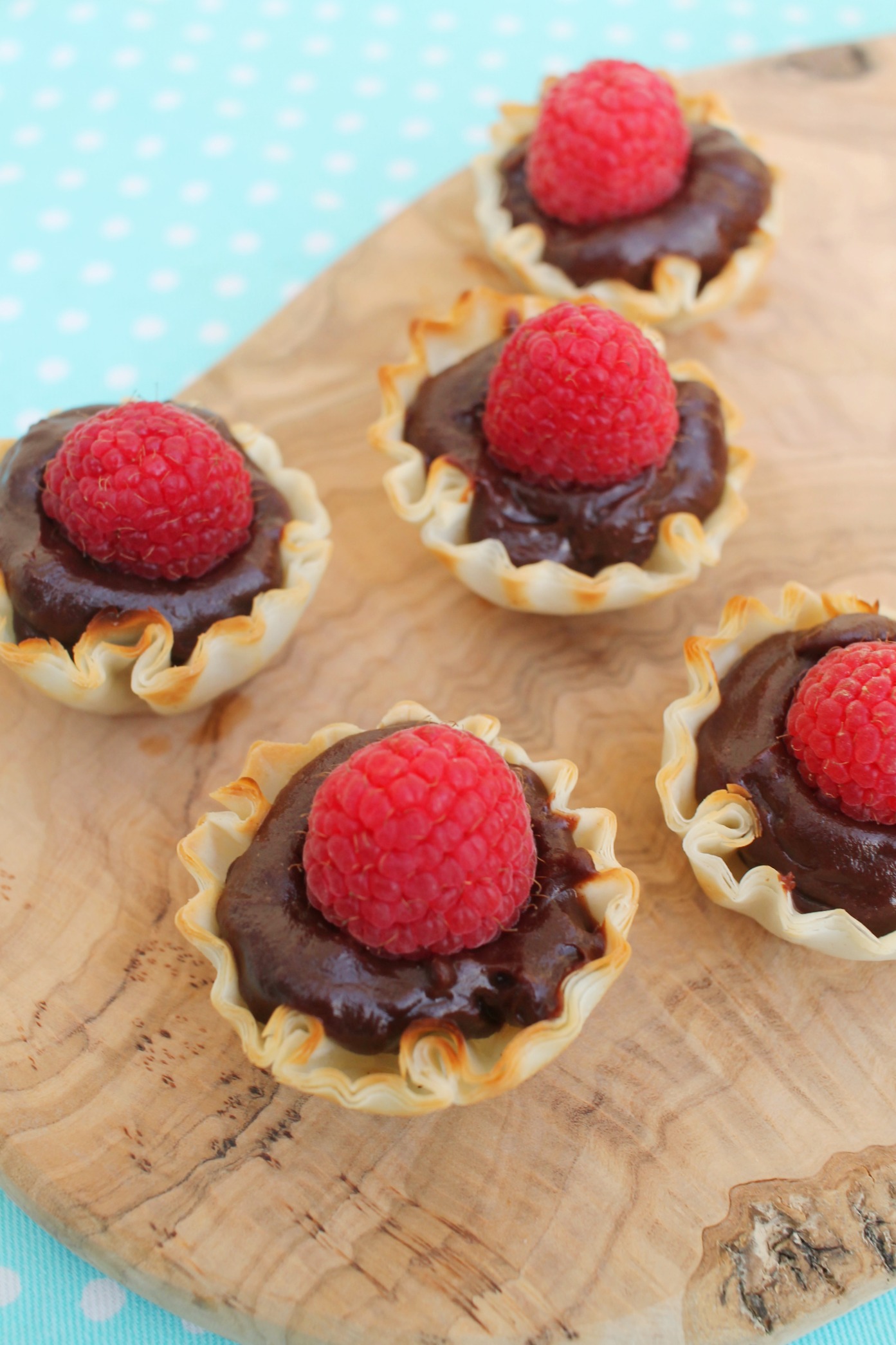 cutting board with phyllo tart shell filled with chooclate ganache and topped with a raspberry