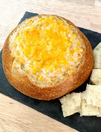 a bread bowl hollowed out and filled with a hot corn dip with cubes of bread beside it