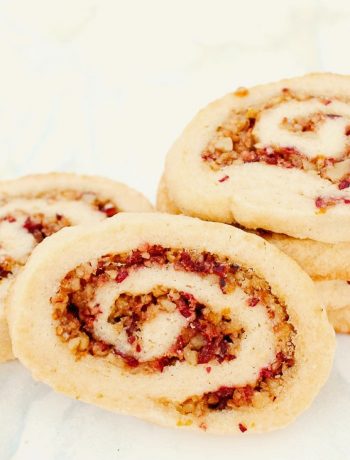 up close shot of a cranberry walnut pinwheel cookie with more stacked behind it