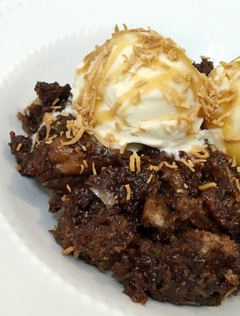white bowl with German chocolate bread pudding topped with vanilla ice cream, toasted coconut and caramel sauce