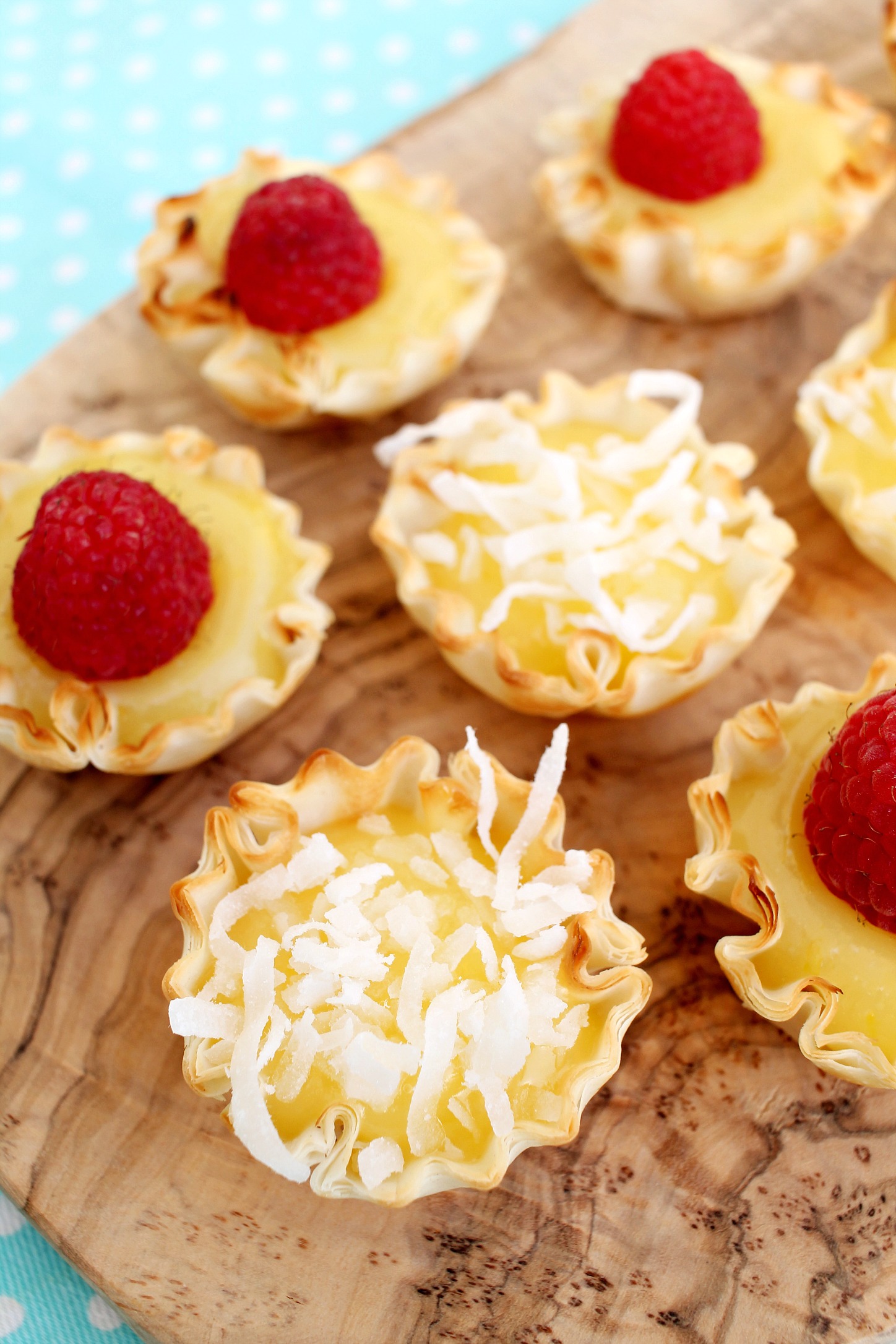 cutting board with lemon curd filled mini tart shells topped with raspberries and shredded coconut