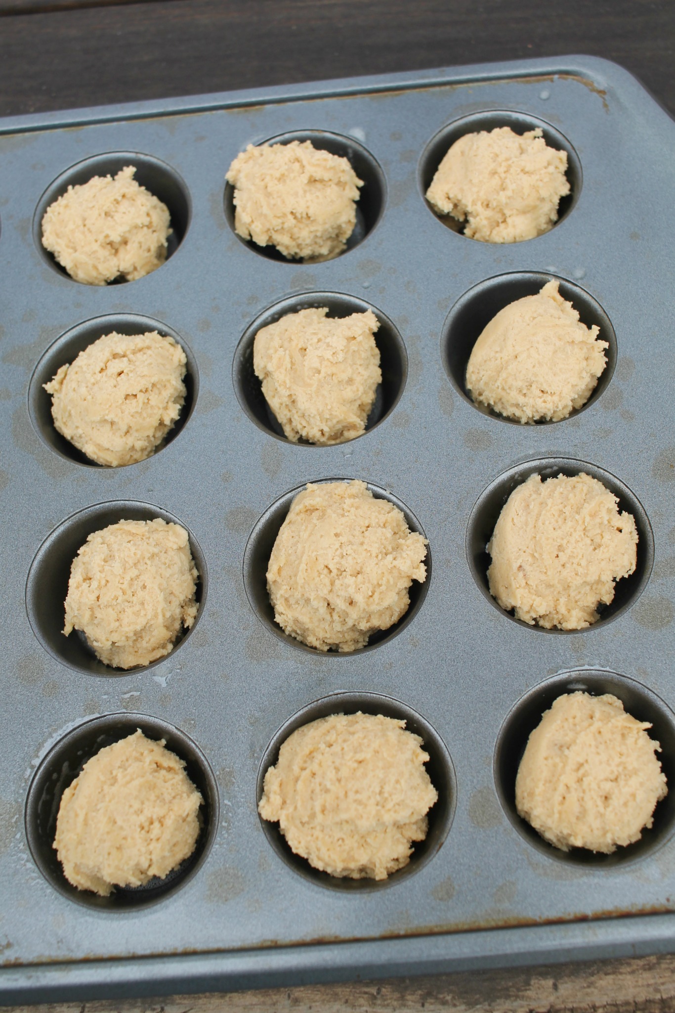 a mini muffin tin with balls of peanut butter dough in the cavity