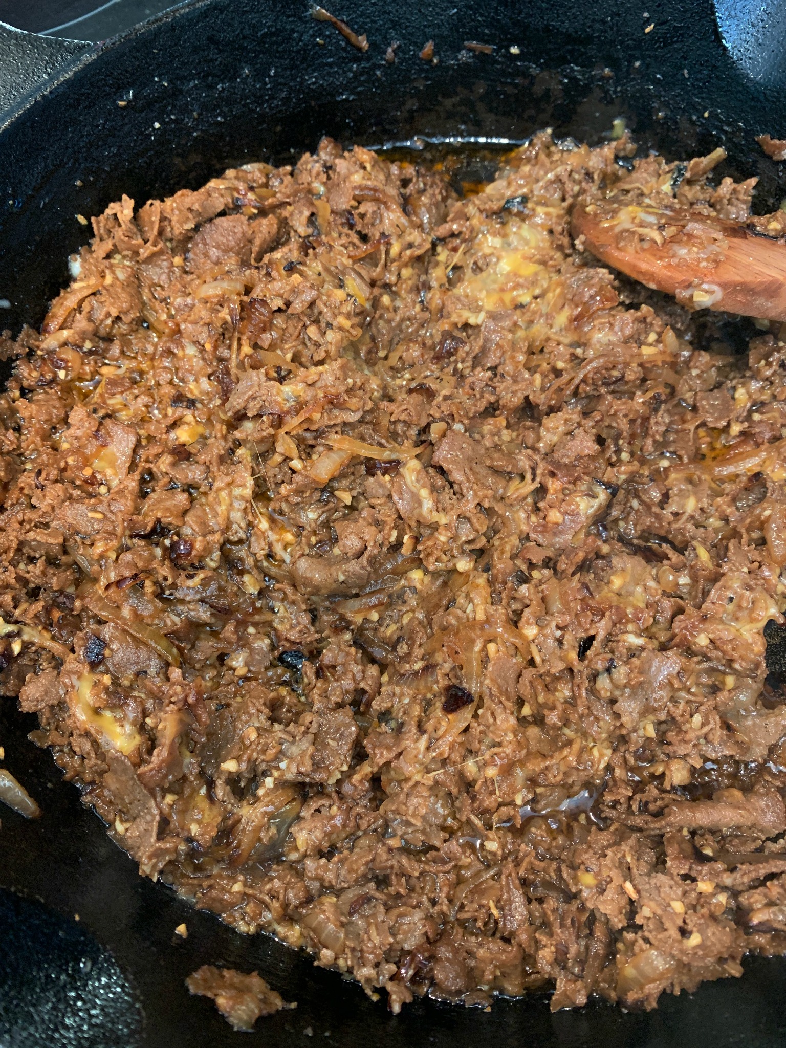 a frying pan with cheesesteak ingredients and a wooden spoon