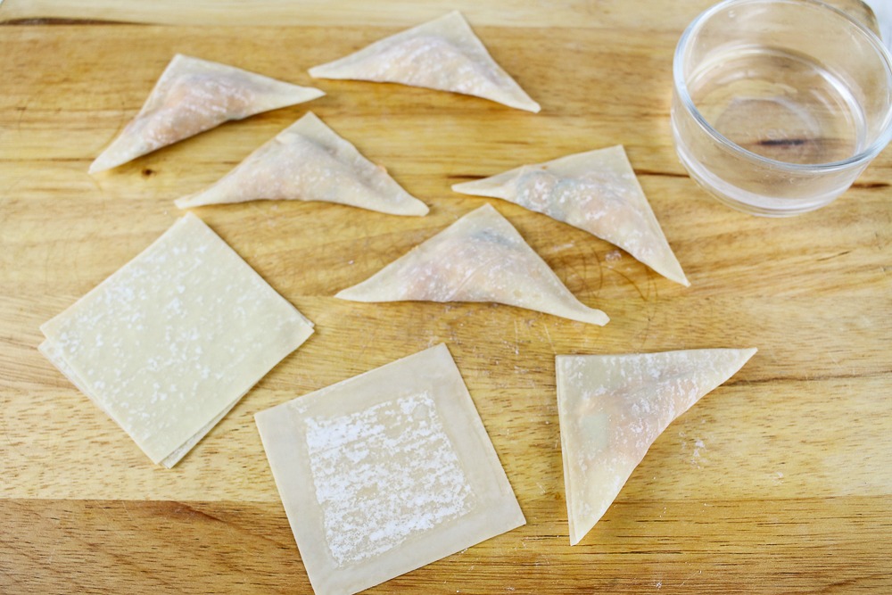 cutting board with pizza wontons, some are already made and filled and some are just the wonton wrappers