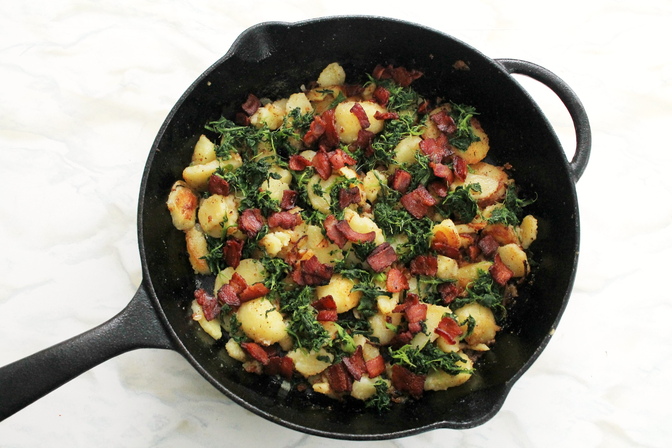 cast iron pan with cooked potatoes, bacon and spinach