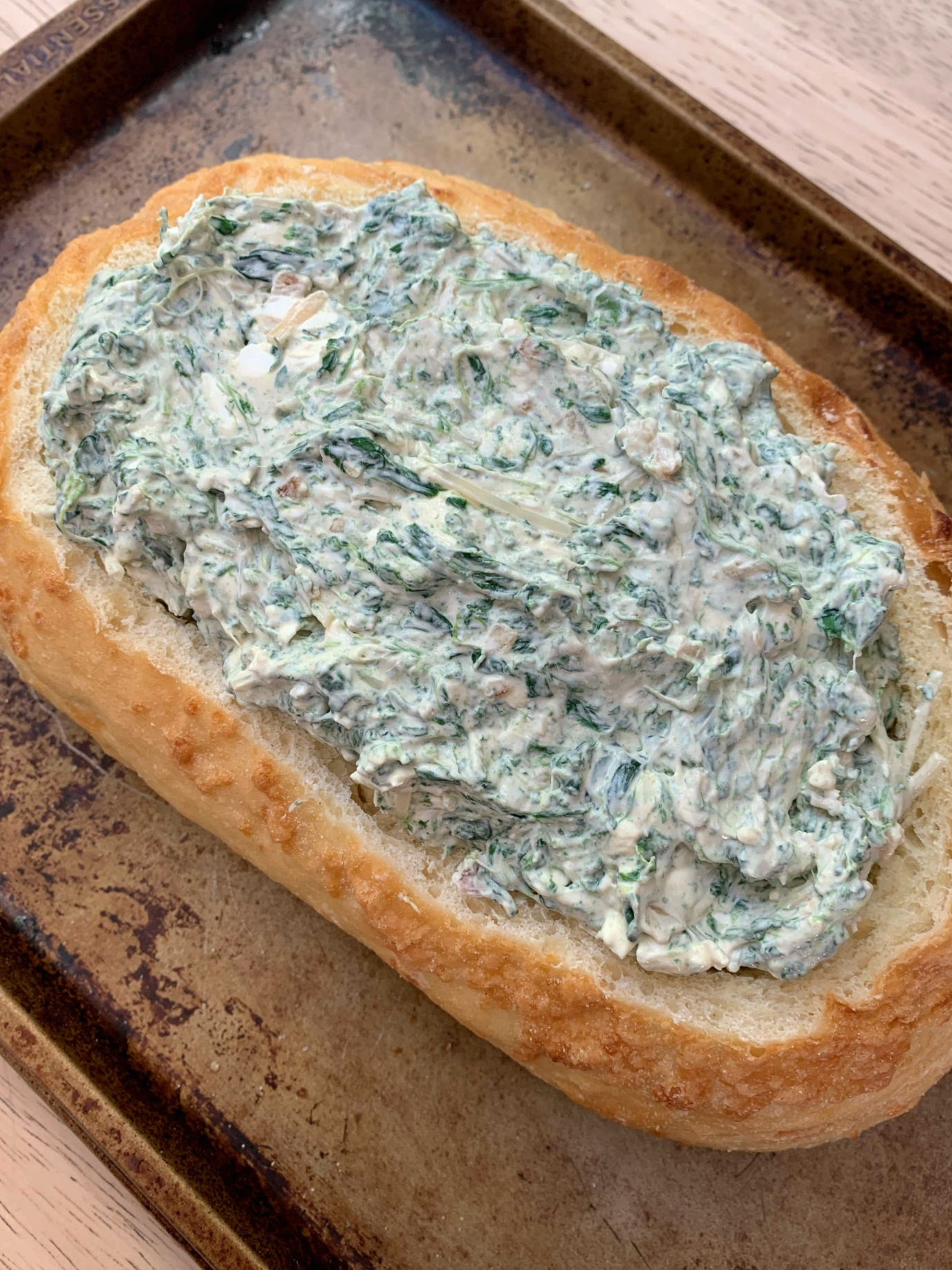 a cookie sheet with an oval loaf of bread hollowed out that's filled with spinach dip