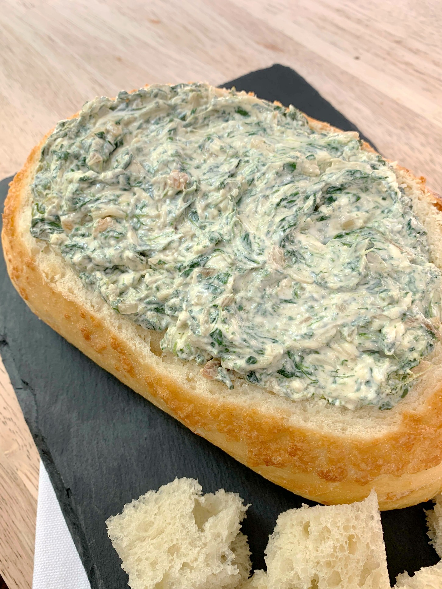 an oval loaf of bread filed with spinach dip on a piece of slate