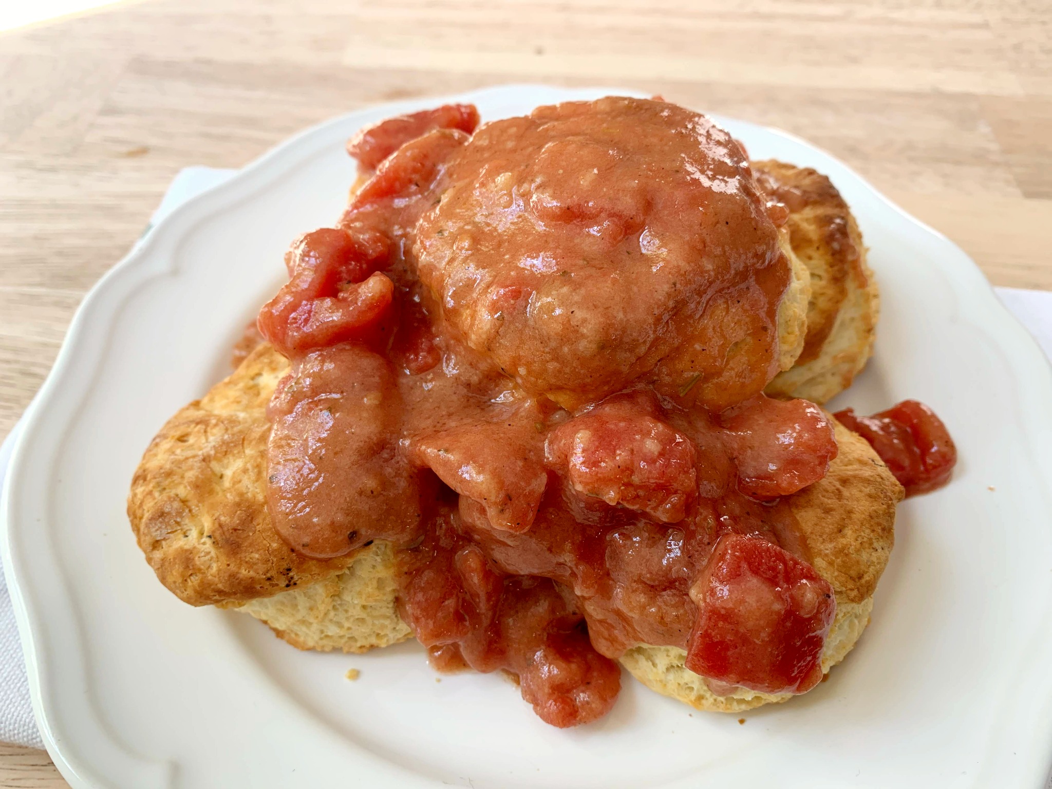 3 buttermilk biscuits on a white plate covered in tomato gravy