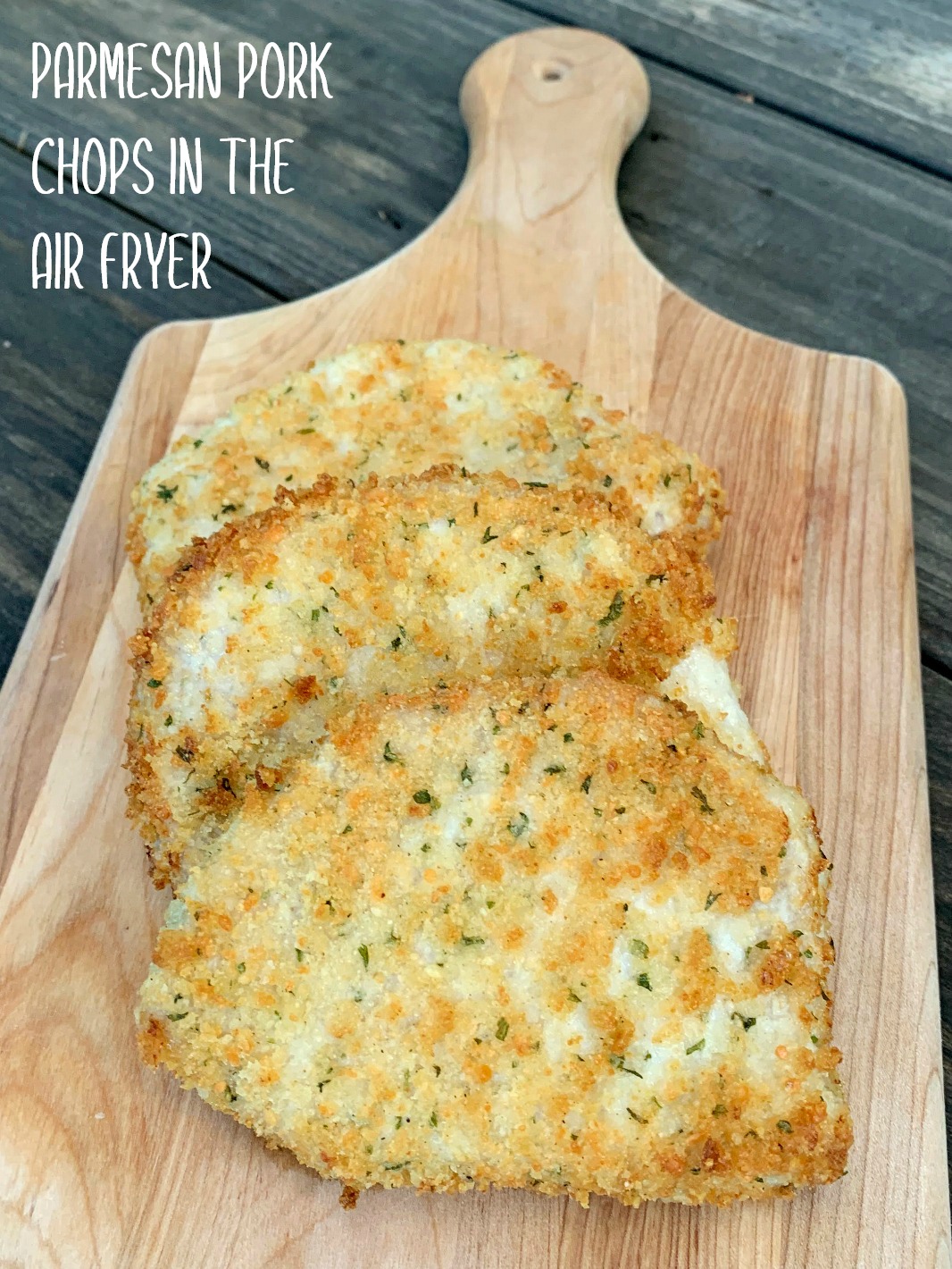 a wooden cutting board with 3 parmesan crusted pork chops