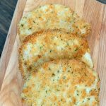 a wooden cutting board with 3 parmesan crusted pork chops