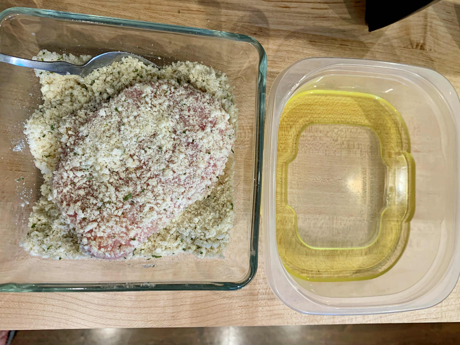 a glass bowl with panko and parmesan and pork chop in it beside a container with vegetable oil
