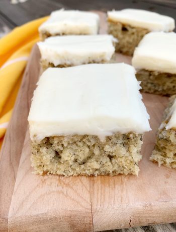 wooden cutting board with an upclose shot of a banana cake slice with cream cheese frosting