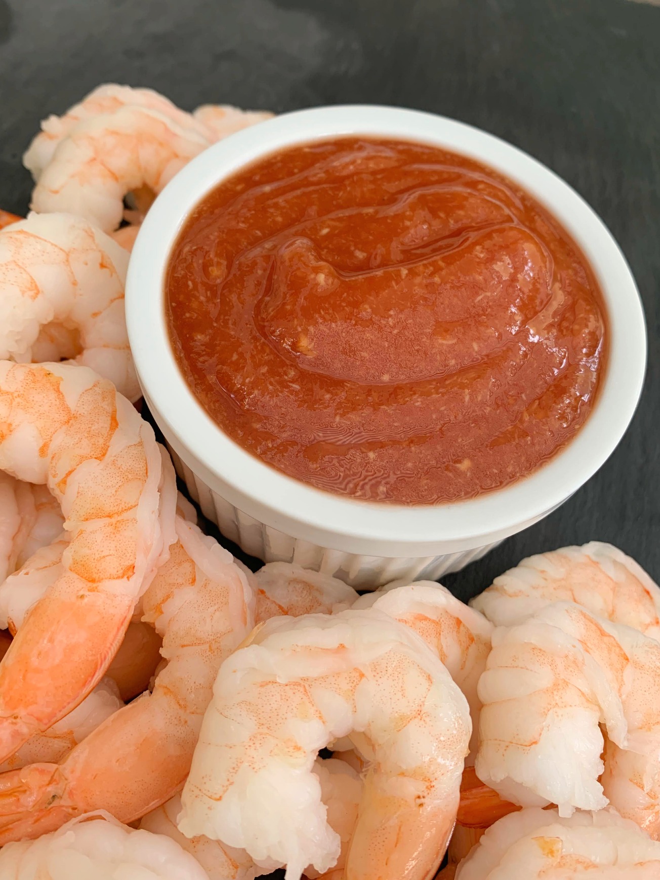 white bowl of cocktail sauce with shrimp around it