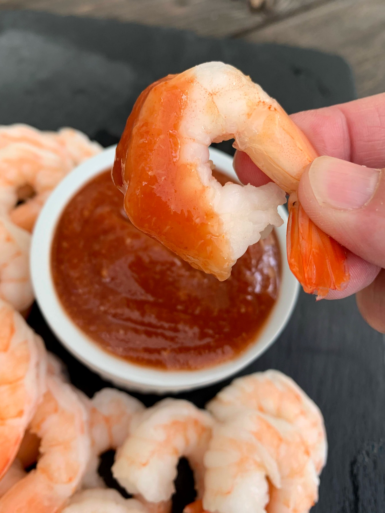 a shrimp being held in the air after dipping it in cocktail sauce