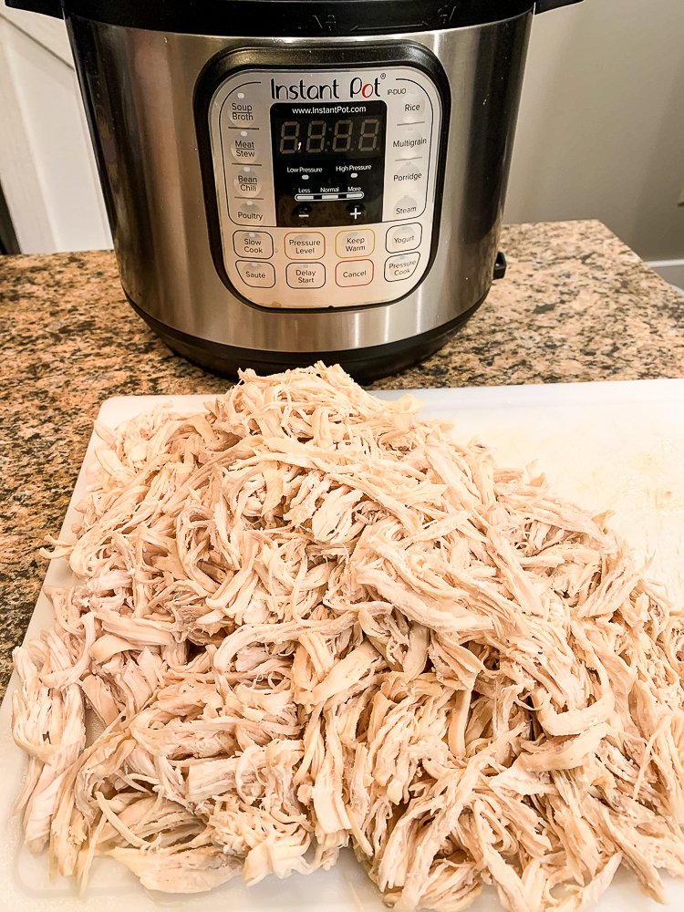 a white cutting board with a pile of shredded chicken and an instant pot in the background