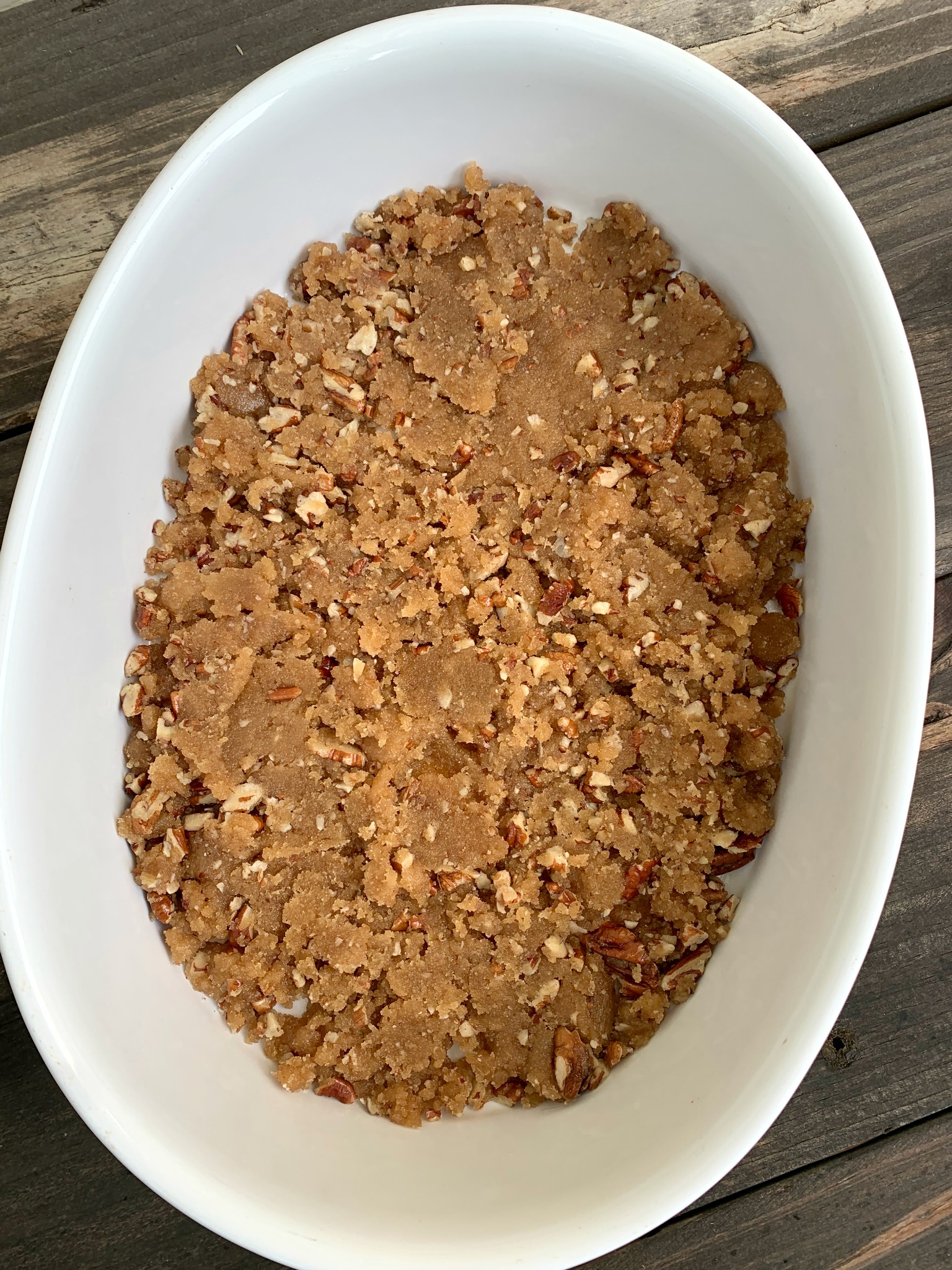 white oval baking dish with brown sugar and pecan mixture sprinkled in the bototm