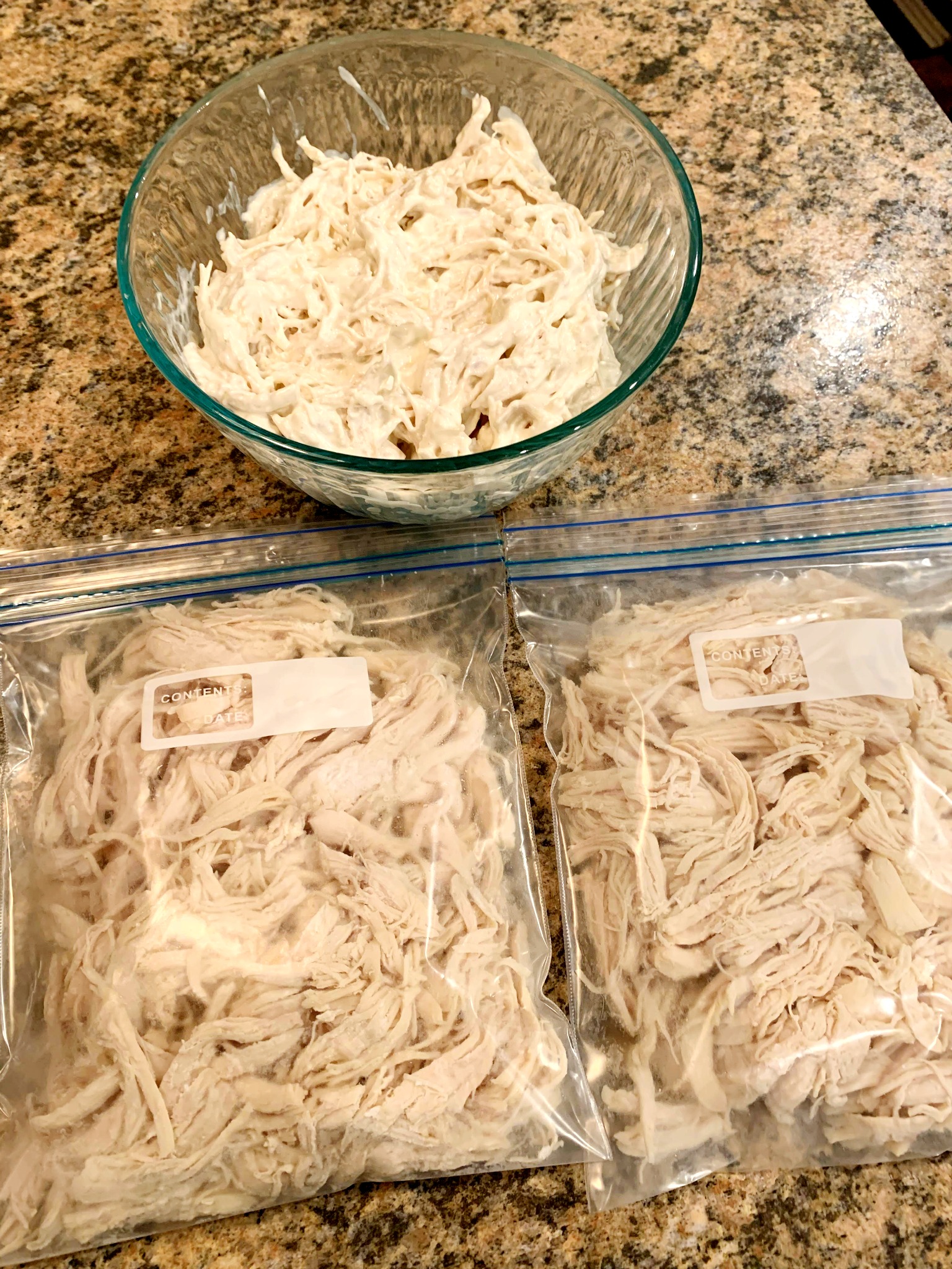a glass bowl of shredded chicken and two freezer bags in front of it filled with shredded chicken