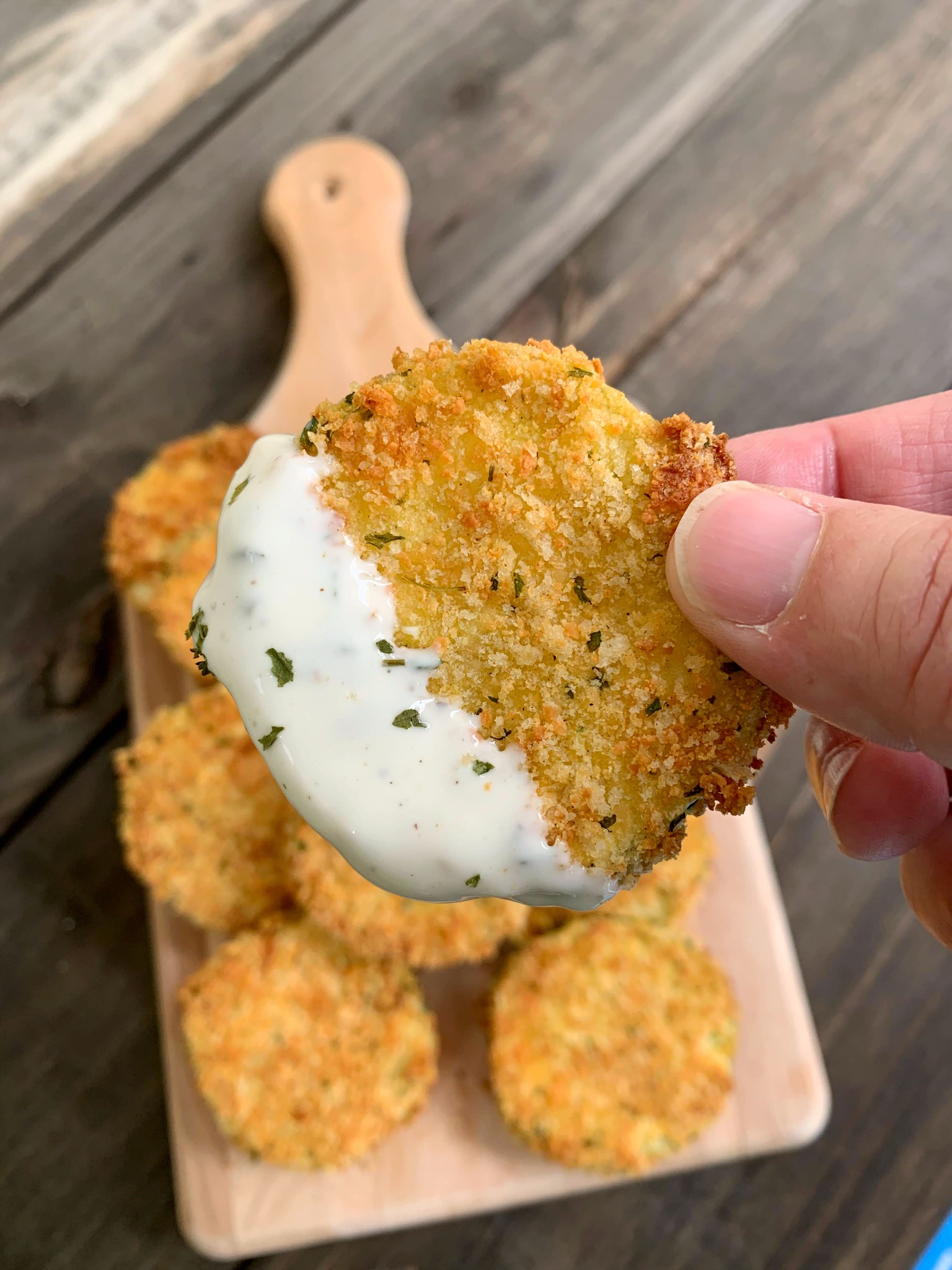 a hand holding a zucchini chip dipped in ranch dressing