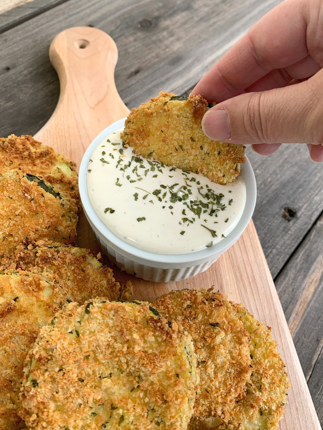 a hand dipping a zucchini chip into a bowl of ranch dressing