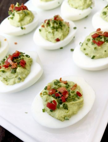 white tray with Avocado Deviled Eggs garnished with chives and bacon bits