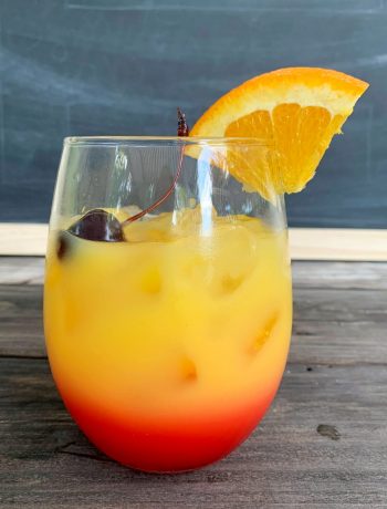 a glass of tequila sunrise with a cherry on top and an orange wedge garnish