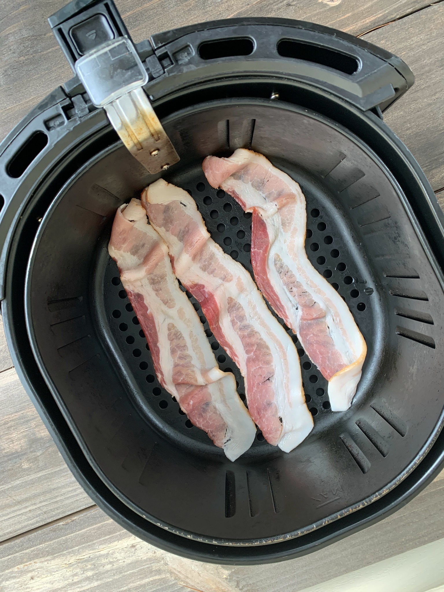 3 raw bacon slices in an air fryer basket