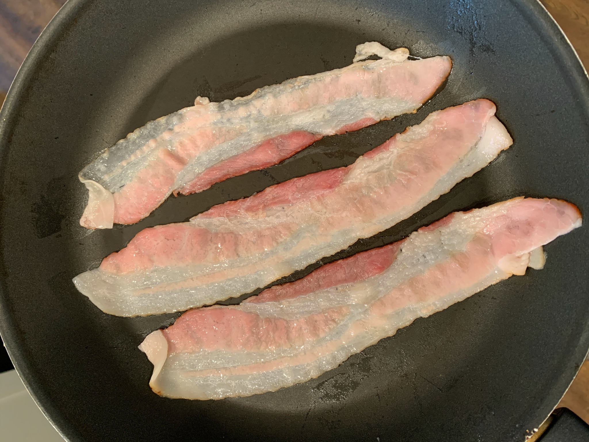 3 strips of raw bacon in a frying pan
