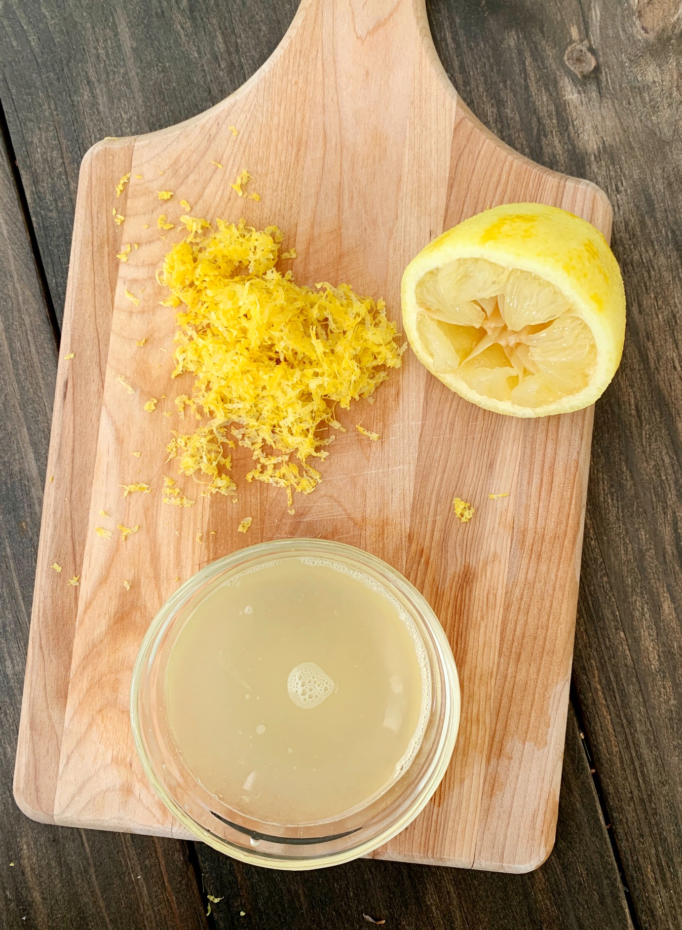 wooden cutting board with a bowl of lemon juice, a pile of lemon zest and a half a lemon that's been juiced