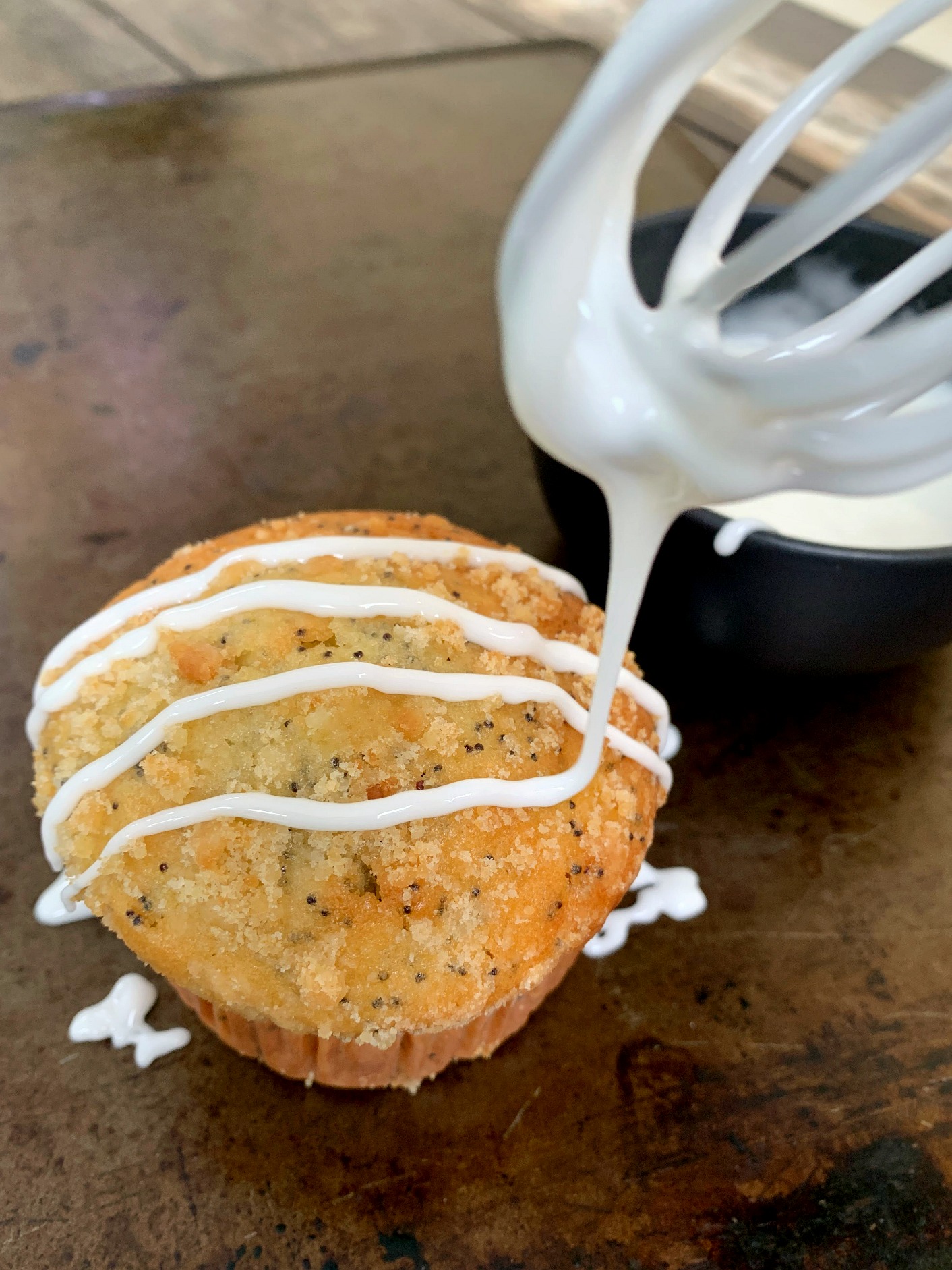 a whisk drizzling glaze on a lemon muffin
