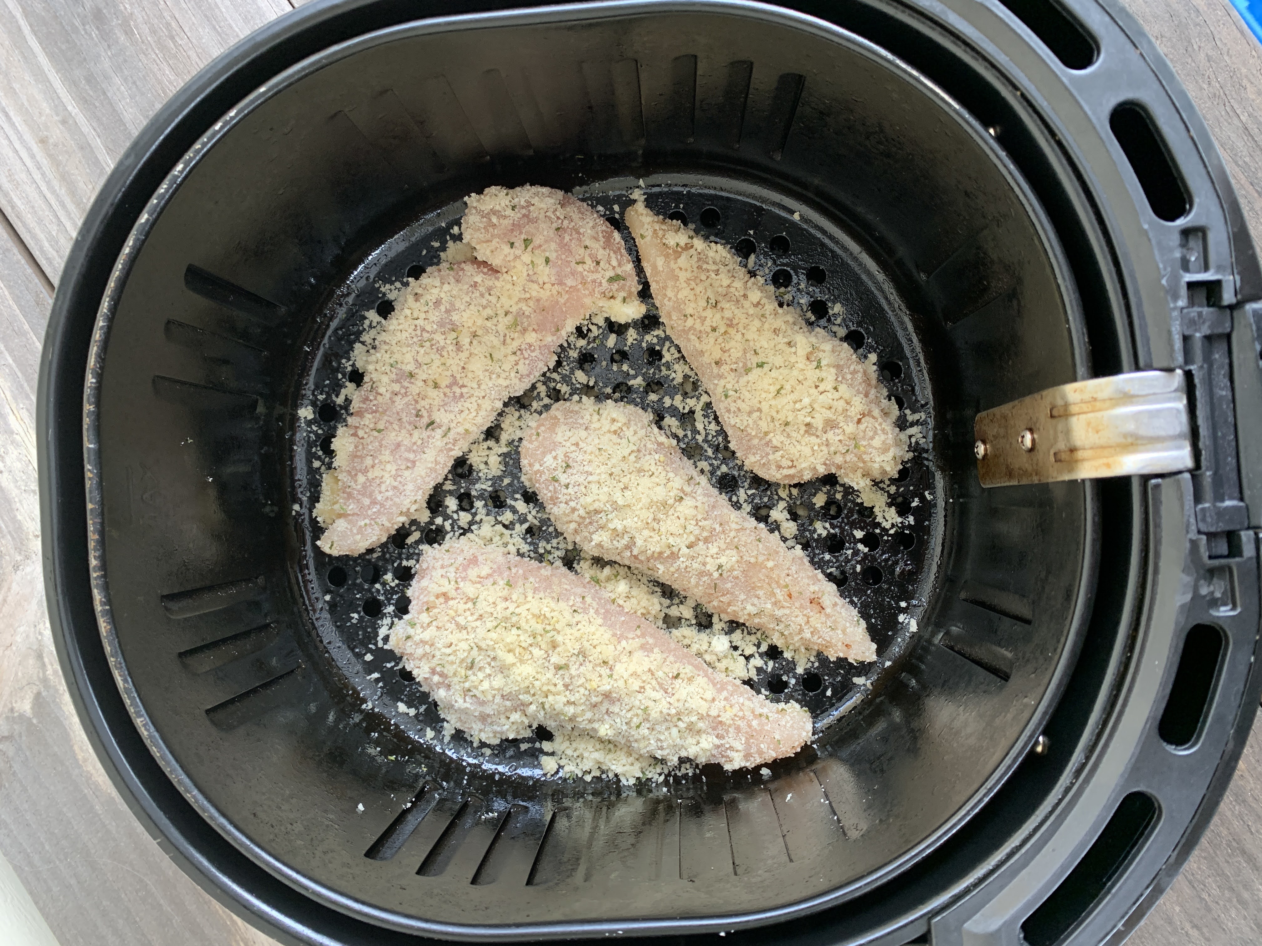 4 uncooked chicken tenders in an air fryer basket