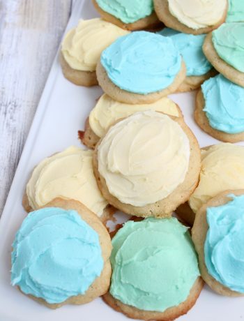 white tray of soft sugar cookies on pile with blue, yellow and green frosting