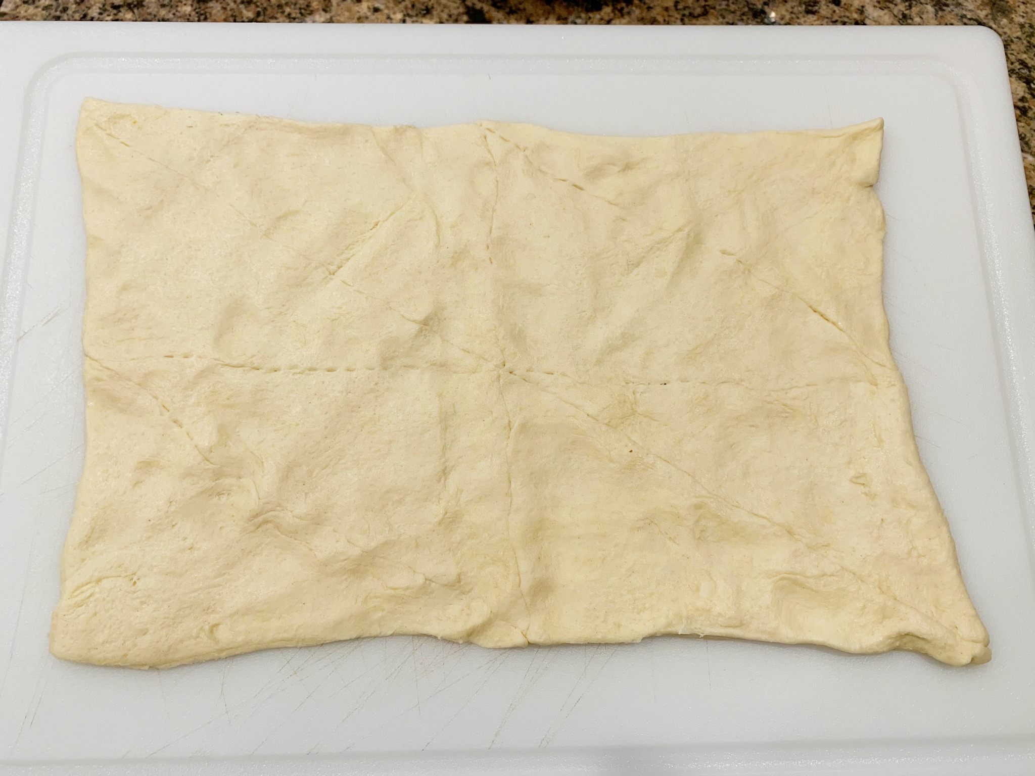 crescent rolls rolled out on a white cutting board with seams pinched togeher